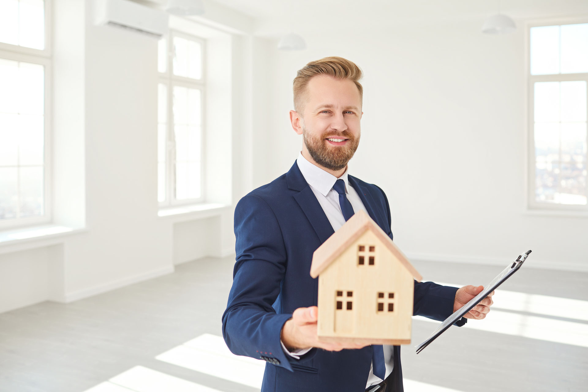 Immobilienmakler hält ein Modell des Hauses lächelnd in weißen Immobilien Zimmer Wohnung nach Hause.